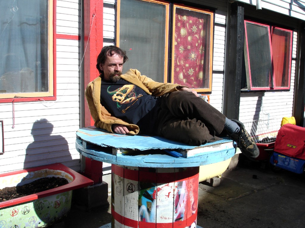 Person reclining on a painted cable spool outside a colourful building